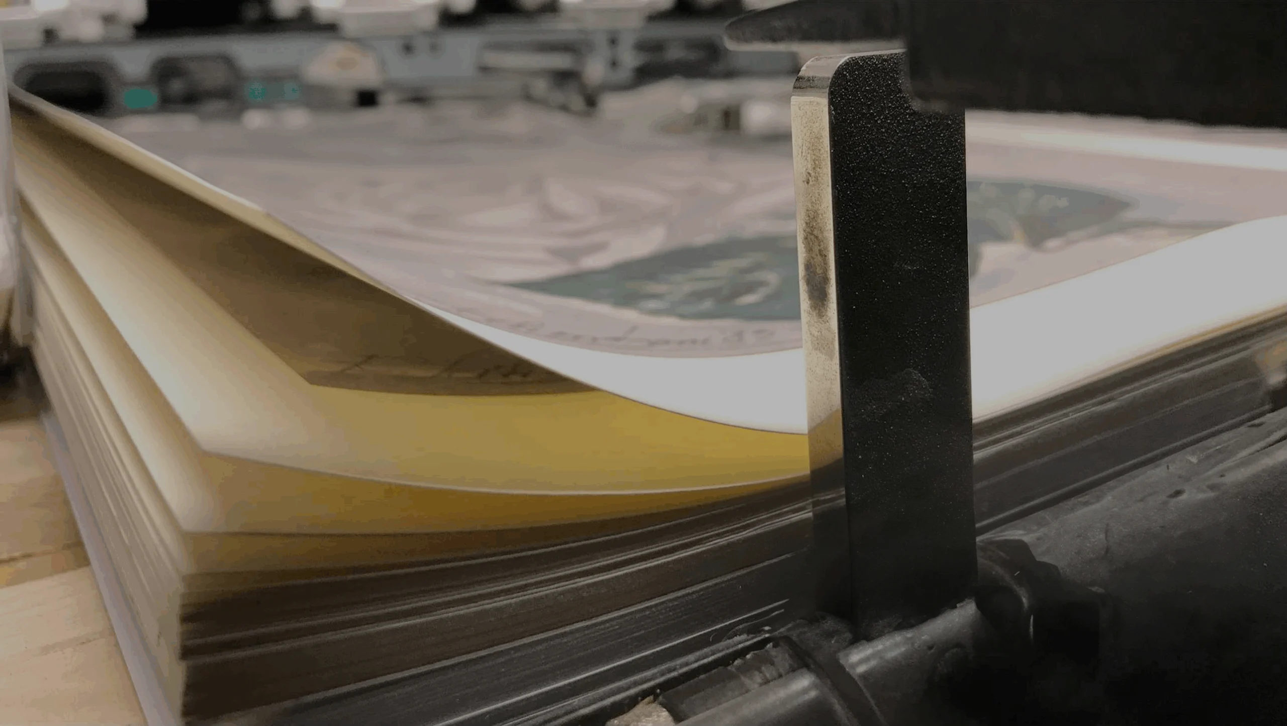 Pila di fogli stampati sotto il fermo metallico di una macchina da stampa, nell'atelier PrintLitoArt